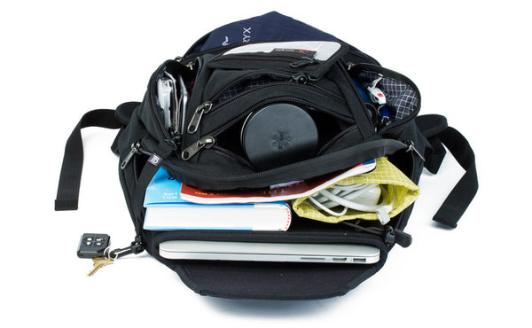 A Synapse 19 with its pockets open, containing a laptop, books, a water bottle, cables, a multitool, and a wallet and other various accoutrements.